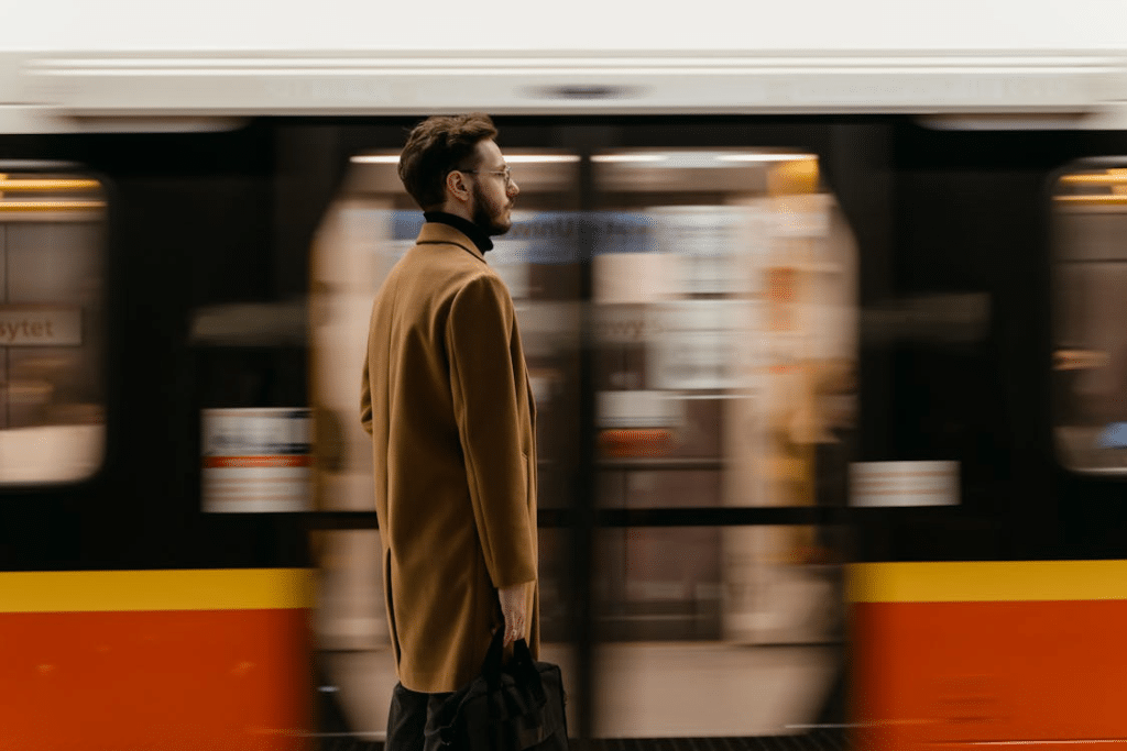 A Man in Brown Coat Standing on a Train Station Near a Moving Train
