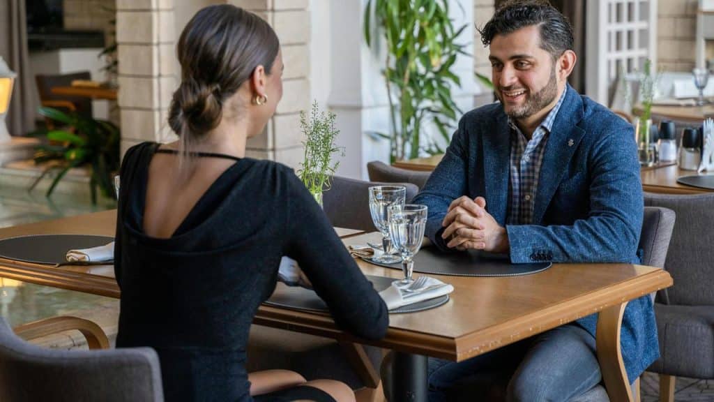 A man and woman sitting at a restaurant table smiling and talking.