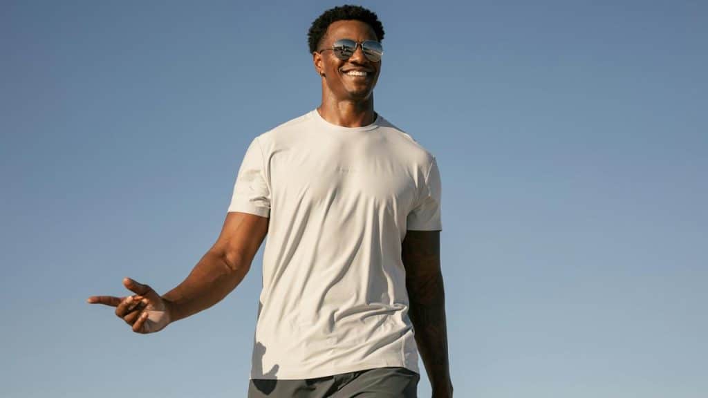 A man smiling and walking outdoors under a clear sky.