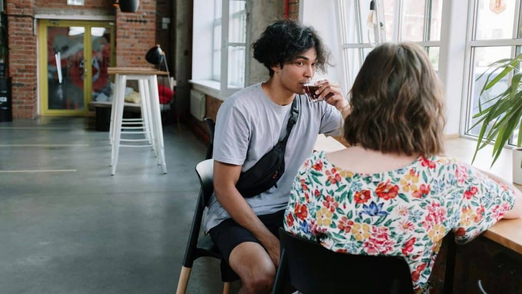 A person drinking a beverage while sitting across from someone in a café.