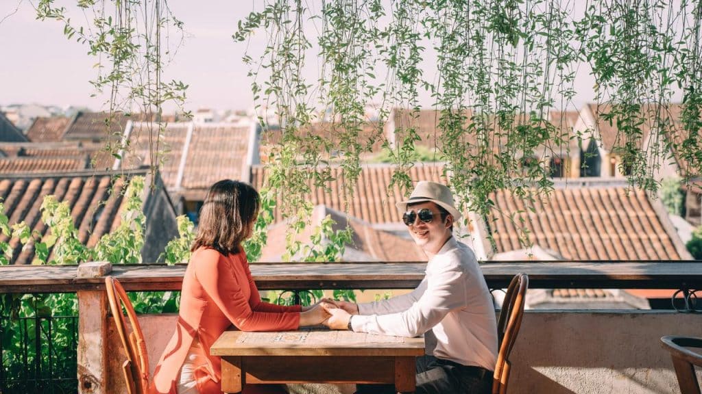 A couple sitting at an outdoor café holding hands under hanging plants.