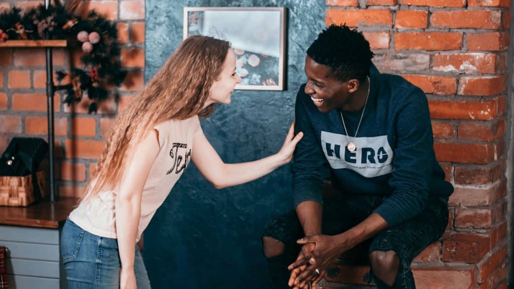 A young Black man and a young white woman laughing together in a room