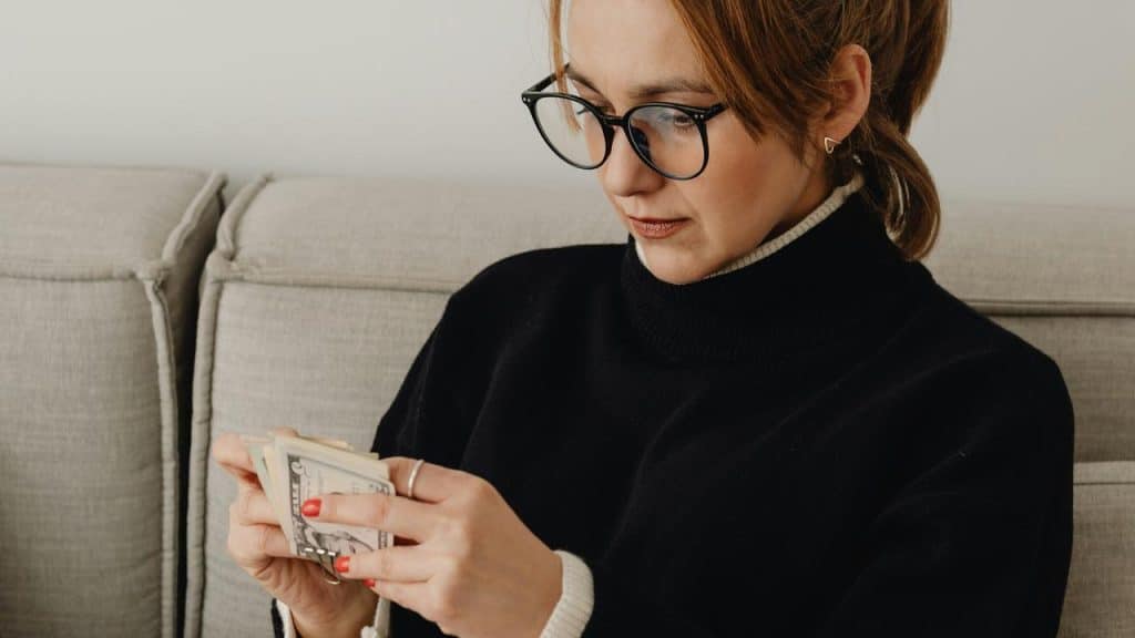 A woman wearing glasses sits on a couch counting money.