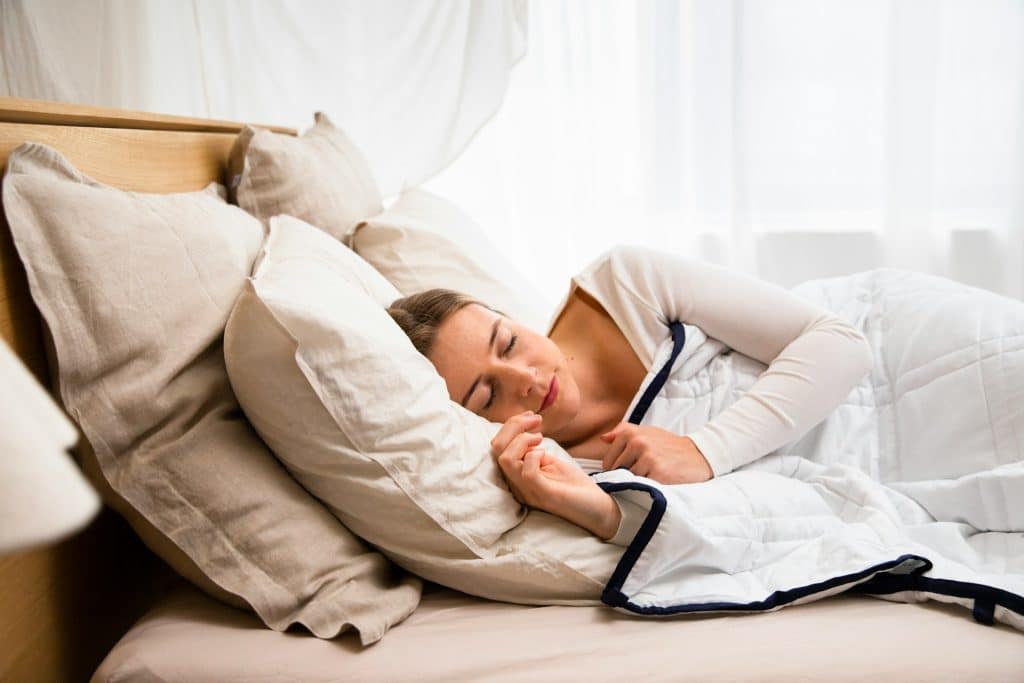 The woman is sleeping in a bed with a white comforter.
