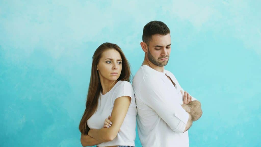 A couple standing back-to-back with arms crossed.