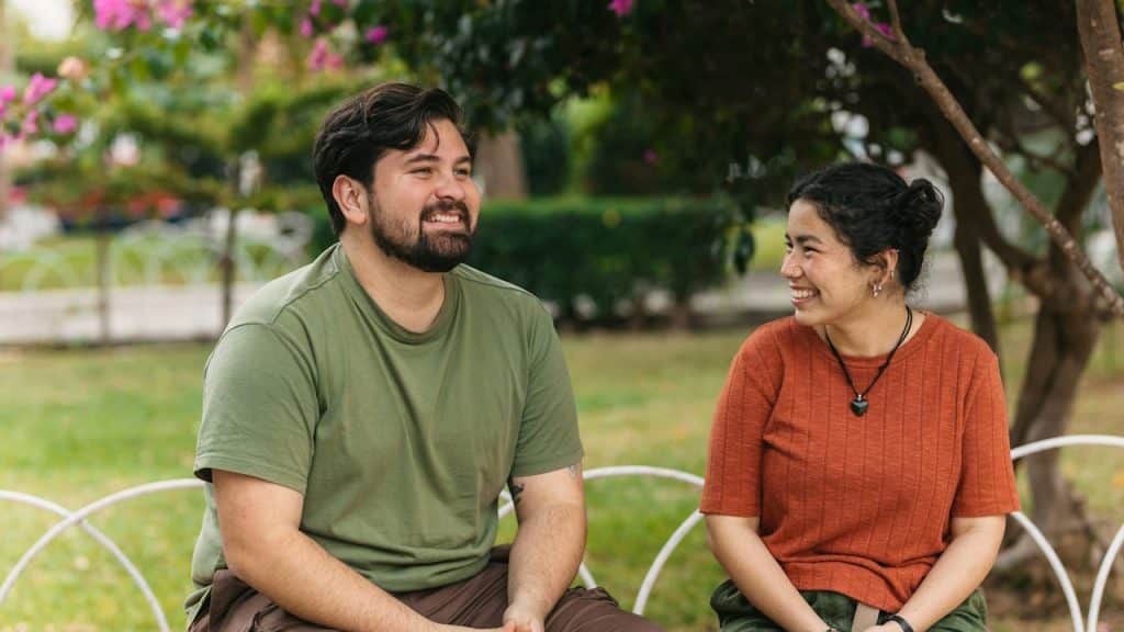 A smiling couple sitting on a bench in a park.