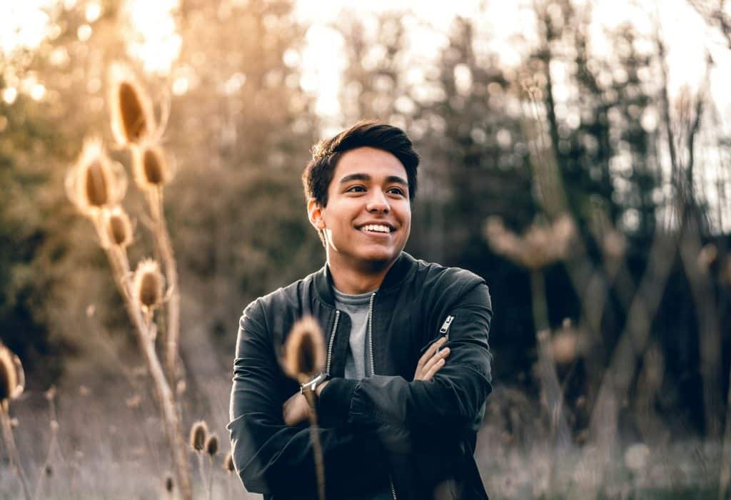 The man standing in the middle of the field is smiling.