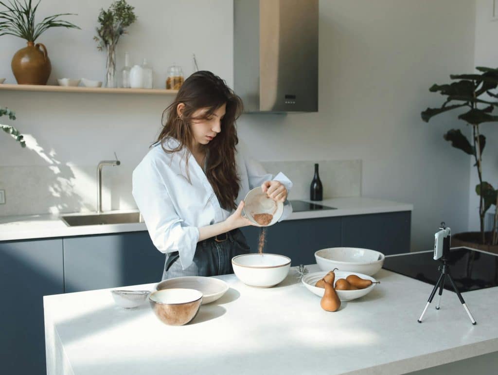 The woman is baking while recording on smartphone.