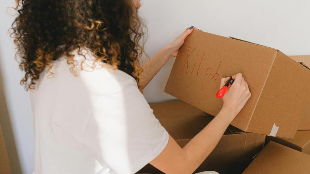 A woman labels a cardboard box with the word “Kitchen.”