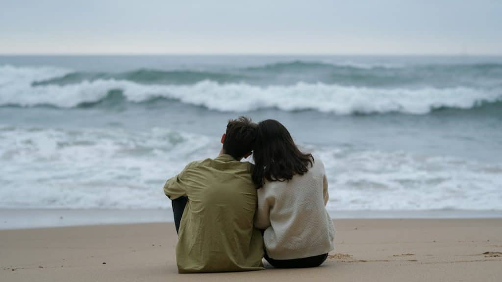 A couple of people sitting on top of a sandy beach.