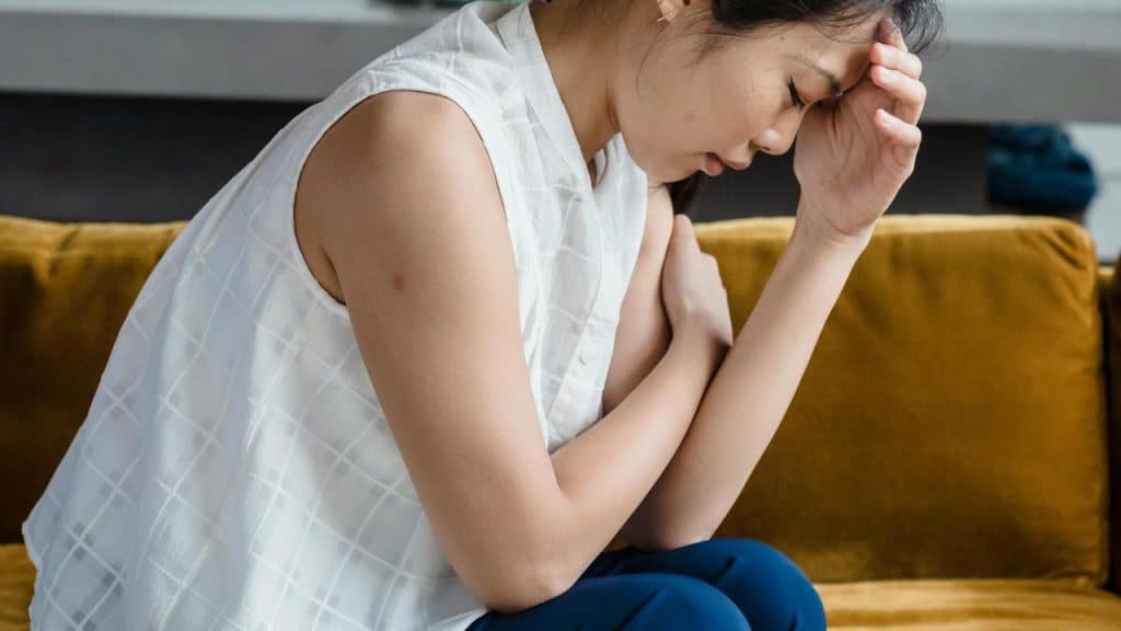 A woman sitting on a couch with her hand on her forehead, looking distressed.