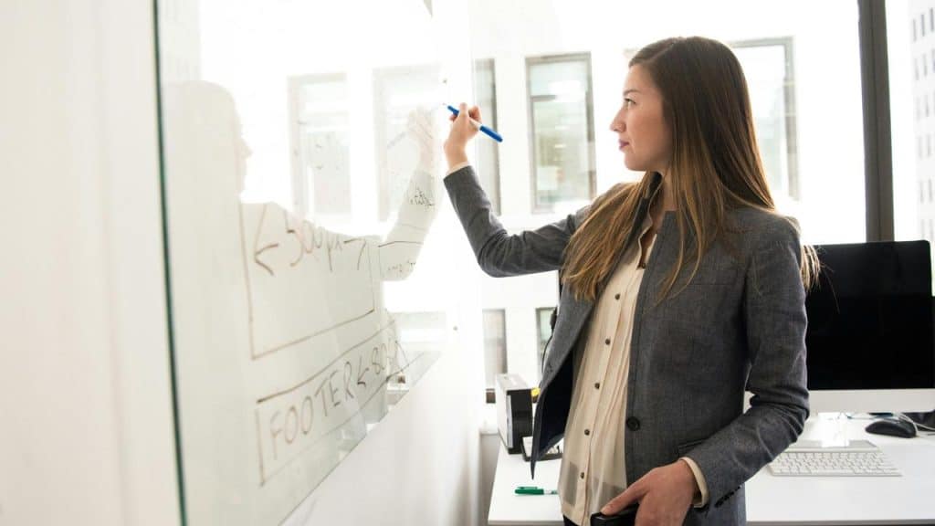A woman writing on a whiteboard in an office setting.