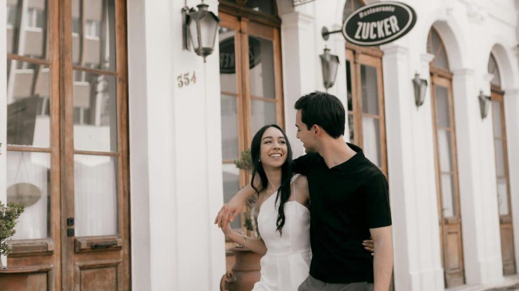 A smiling couple walking arm in arm outside a café.