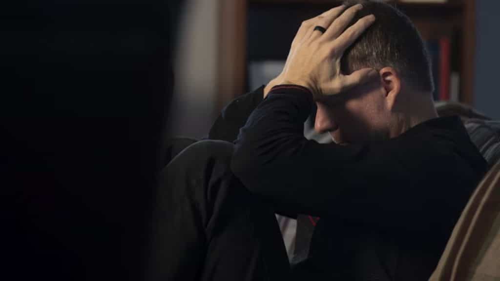 Man sitting on a bed late at night unable to sleep, showing signs of stress