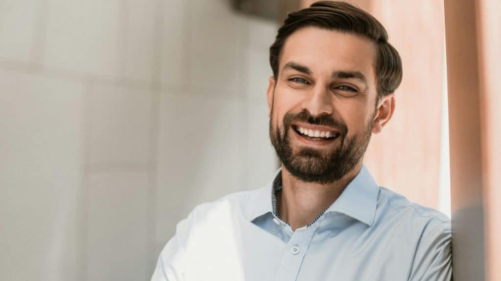 Smiling man with a beard and light blue collared shirt looking directly at the camera.