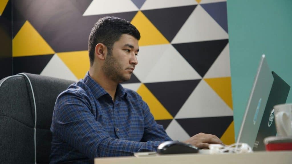 Man in a plaid shirt works on a laptop against a wall with yellow and black triangles