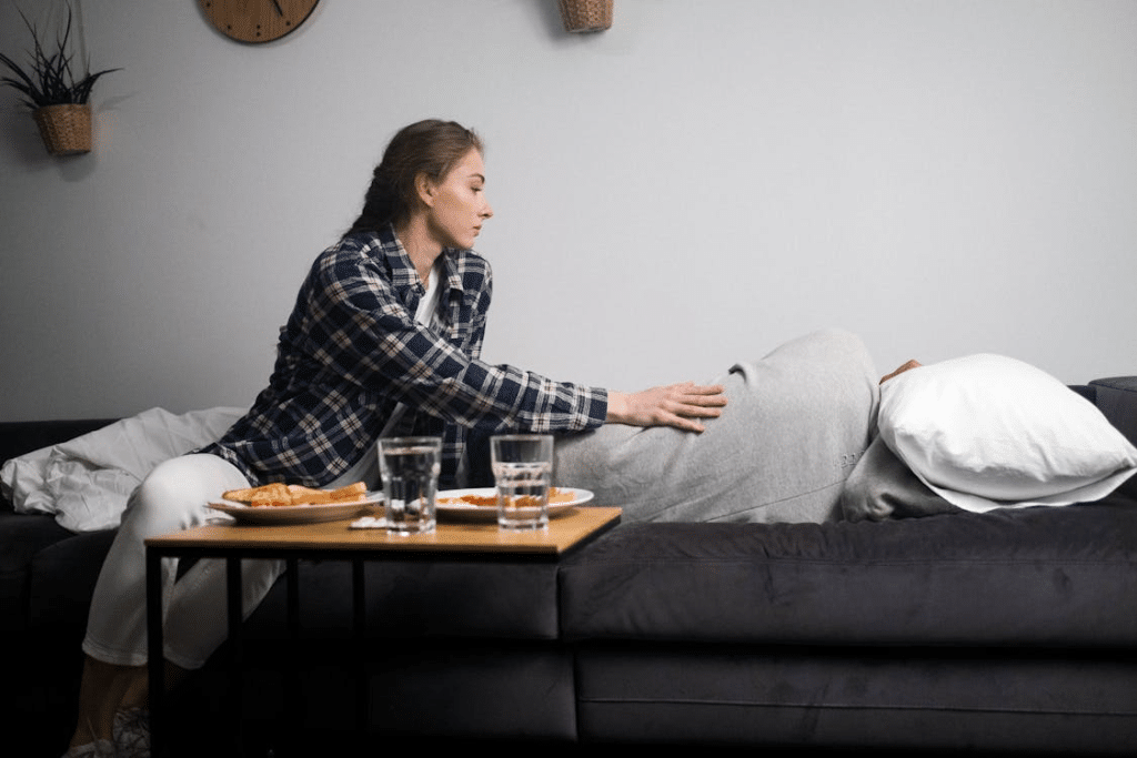 A Woman Sitting Beside a Man lying on the Bed