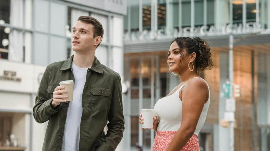 A man and a woman walking outside holding coffee cups.