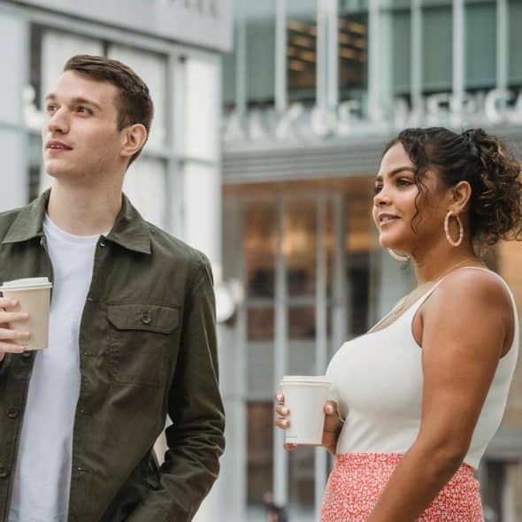 A man and a woman walking outside holding coffee cups.
