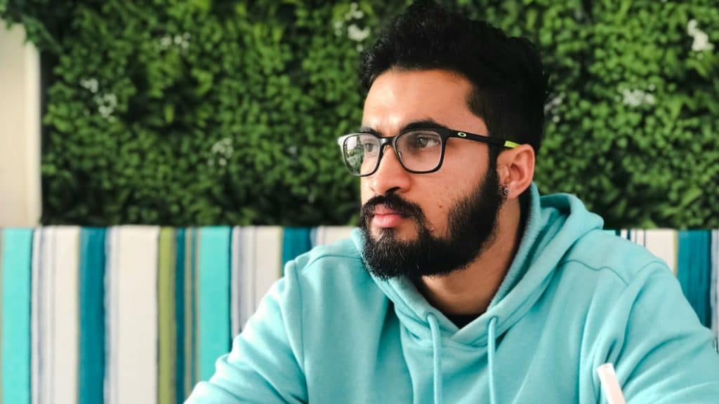 Man with a full beard and glasses wearing a light blue hoodie, looking to the side.