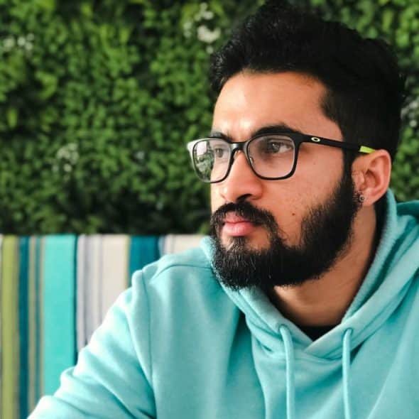 Man with a full beard and glasses wearing a light blue hoodie, looking to the side.