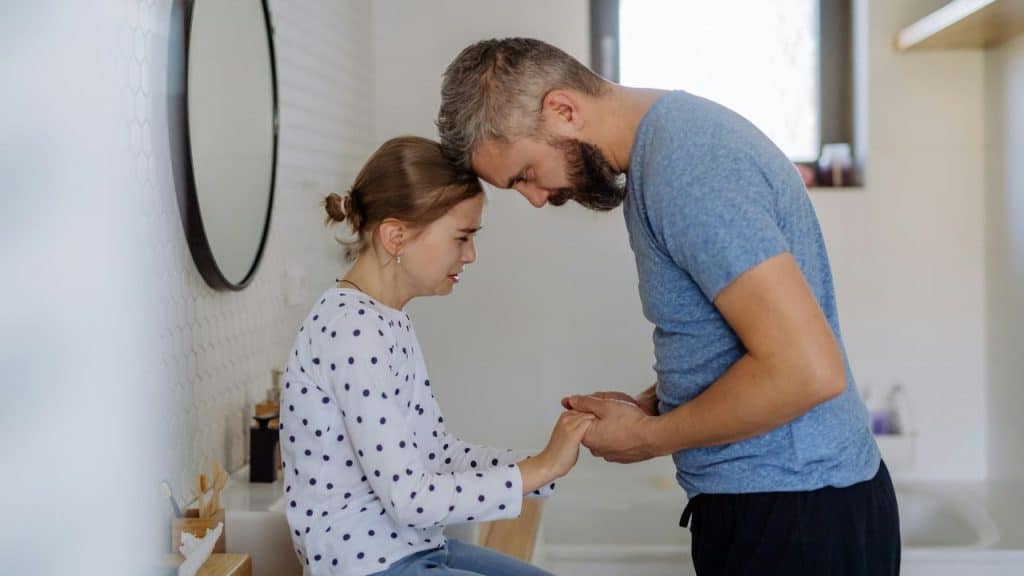 Man and young girl touching foreheads and holding hands in a bathroom.