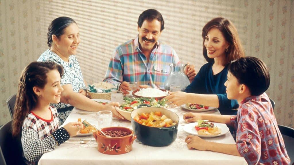 Five smiling people, three adults and two children, eating dinner together at a table.