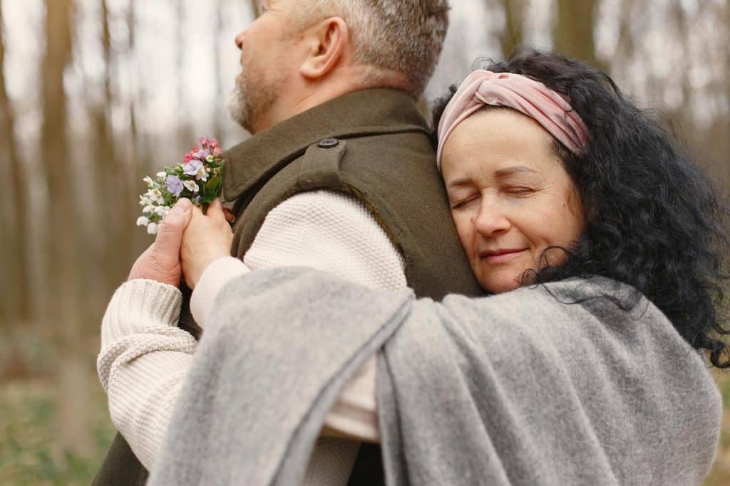 The woman is hugging a man while they’re outdoors.