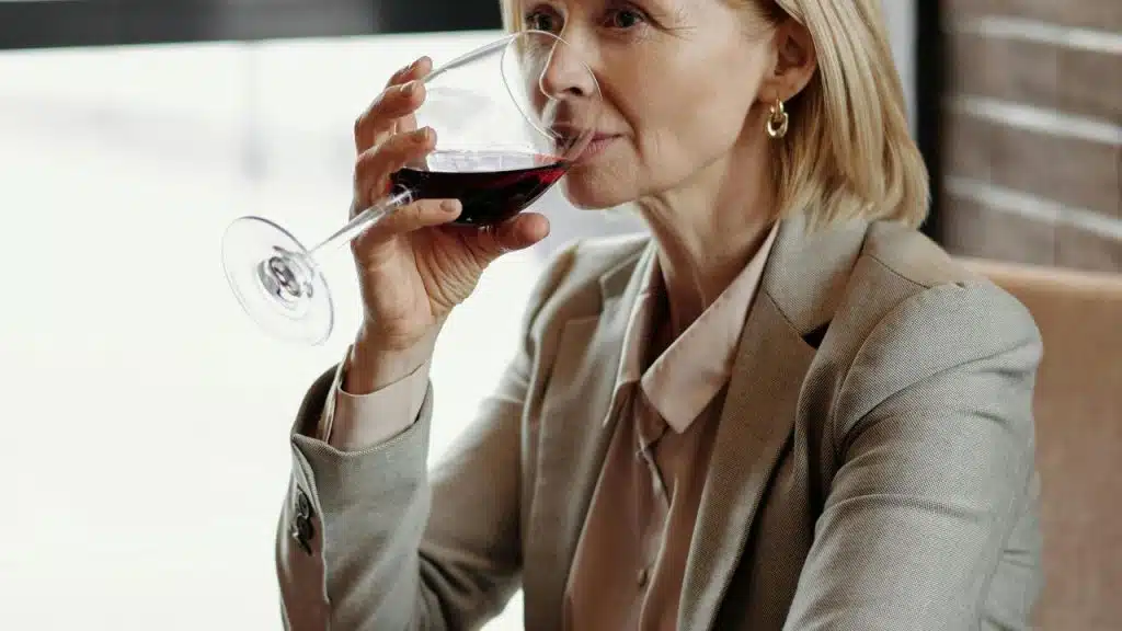 A woman in a beige suit drinking red wine at a restaurant.
