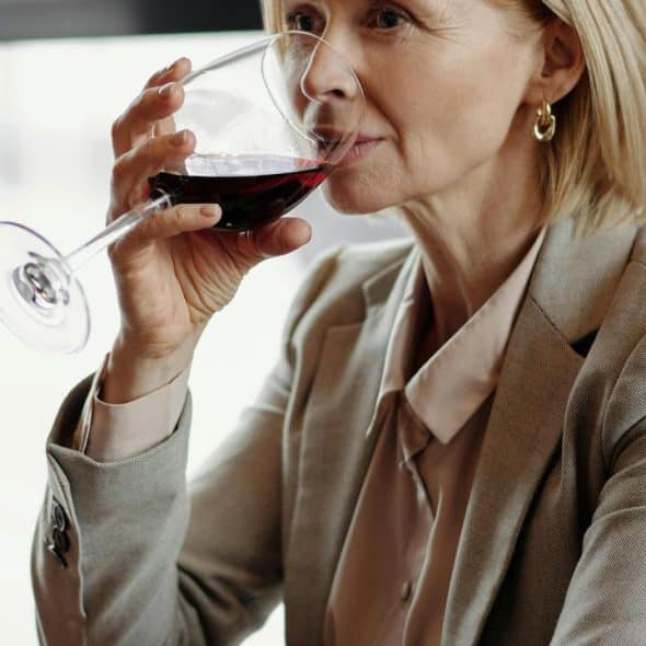 A woman in a beige suit drinking red wine at a restaurant.