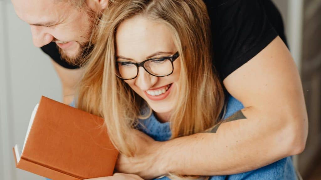 A man hugging a smiling woman who is holding a book.
