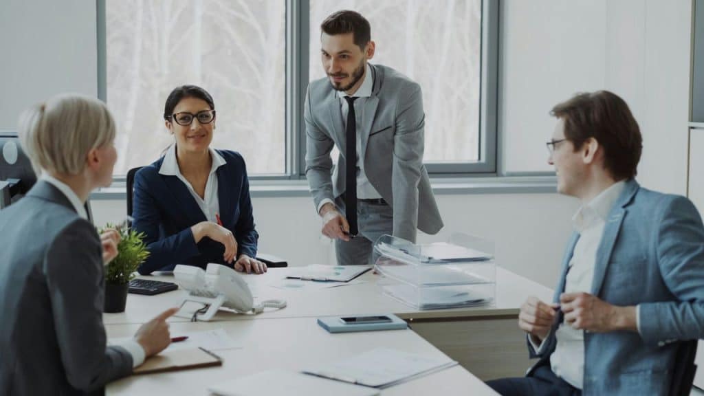 Four professionally dressed adults are meeting around a desk in a well-lit office.
