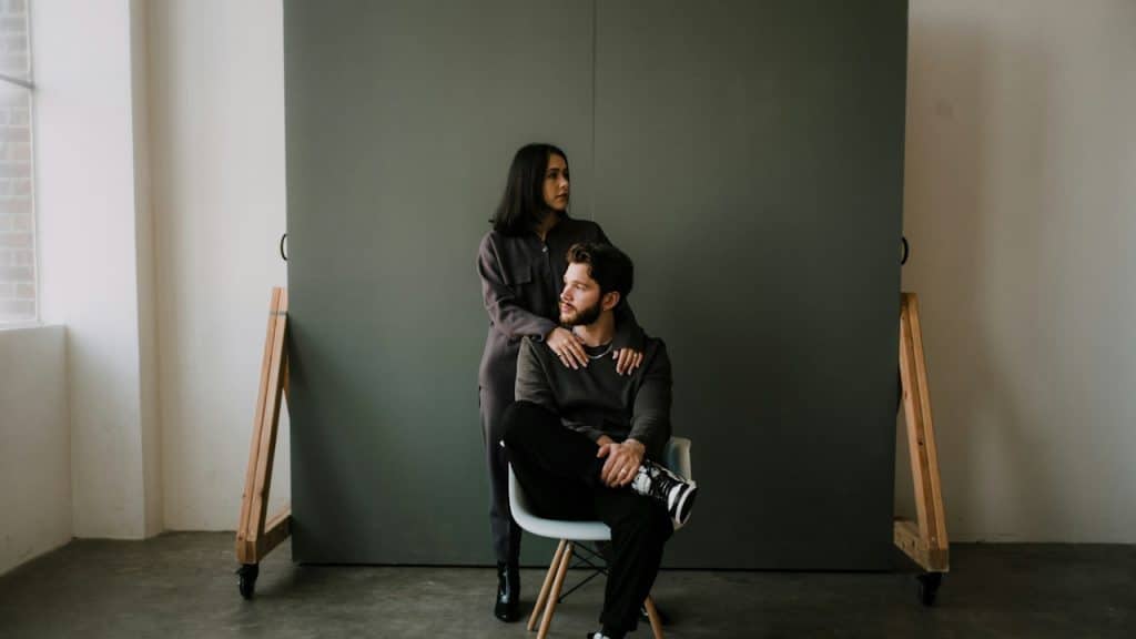 A man is sitting on a chair while a woman is standing behind her.