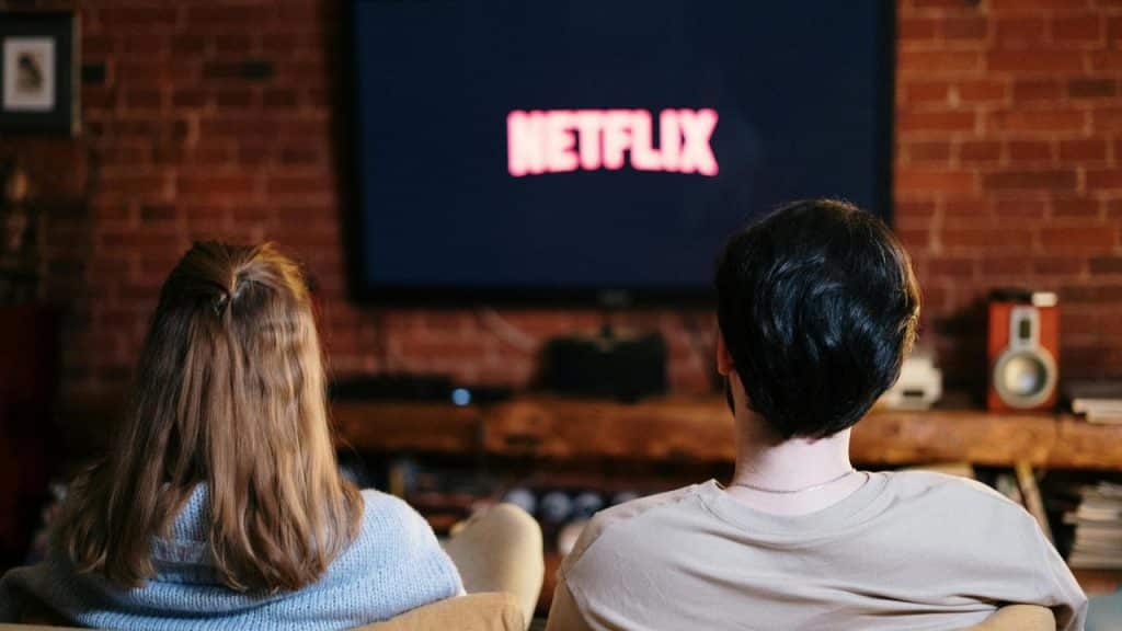 A couple sitting on a couch watching Netflix on a TV.