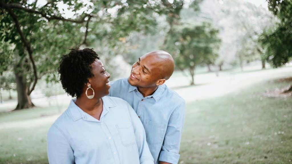 A couple smiling and looking at each other while standing in a park.