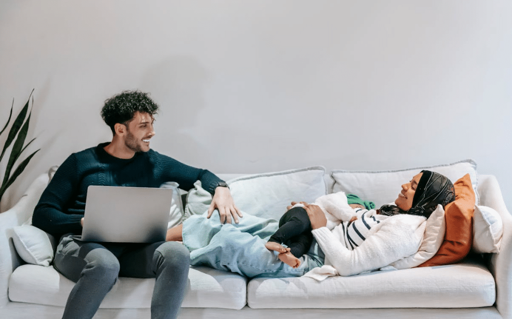 Happy man using laptop while sitting near relaxing wife and baby