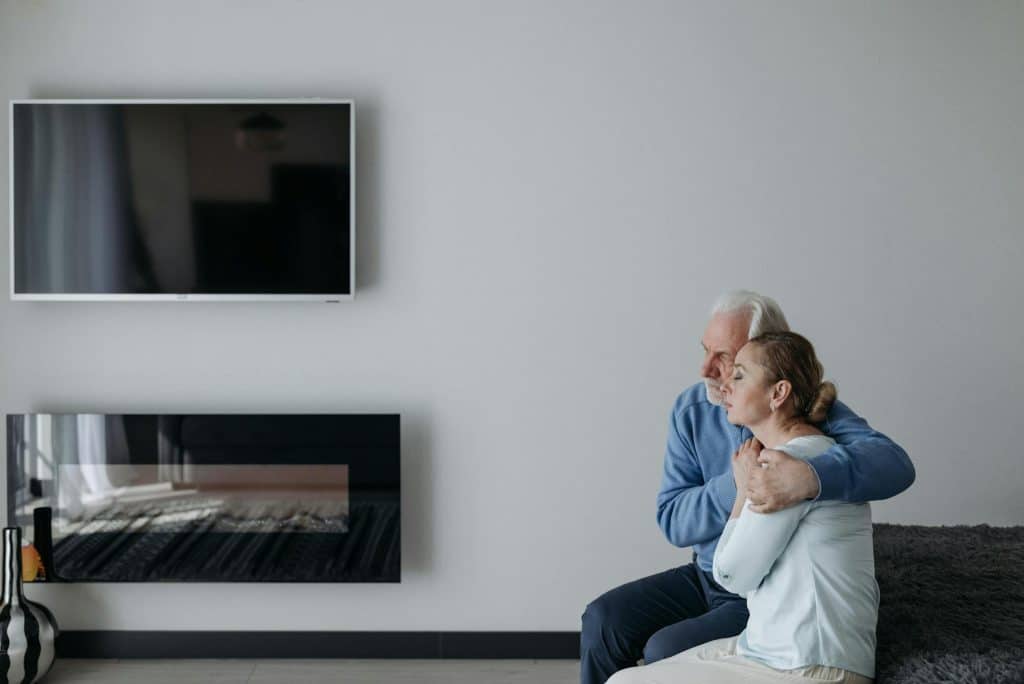 The elderly couple is sitting together and embracing each other.