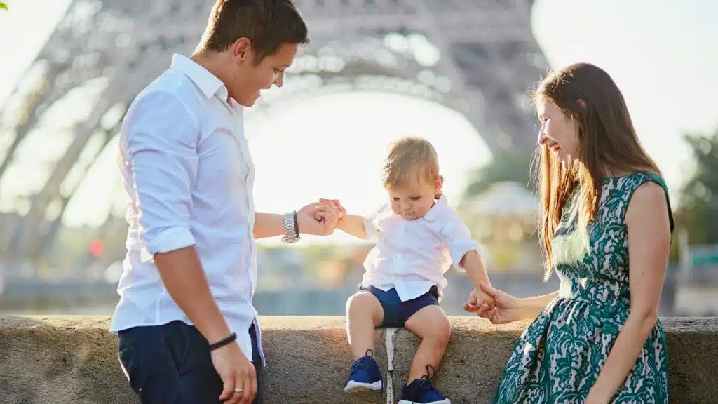 A smiling young family of three with the Eiffel Tower in the background.