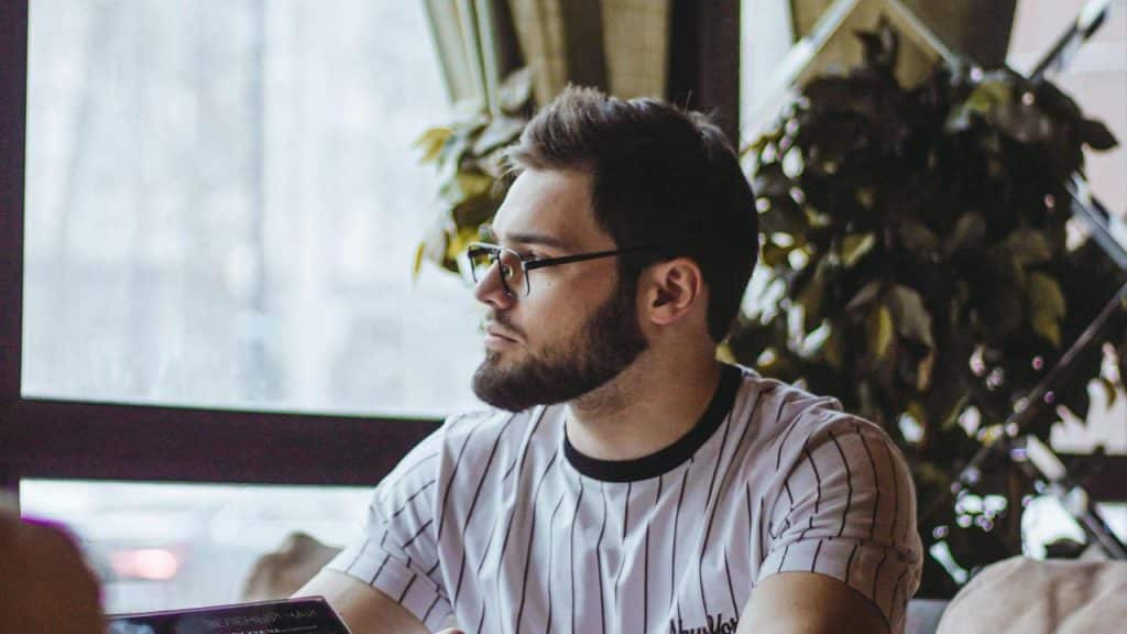 A man wearing glasses sitting indoors and looking to the side.