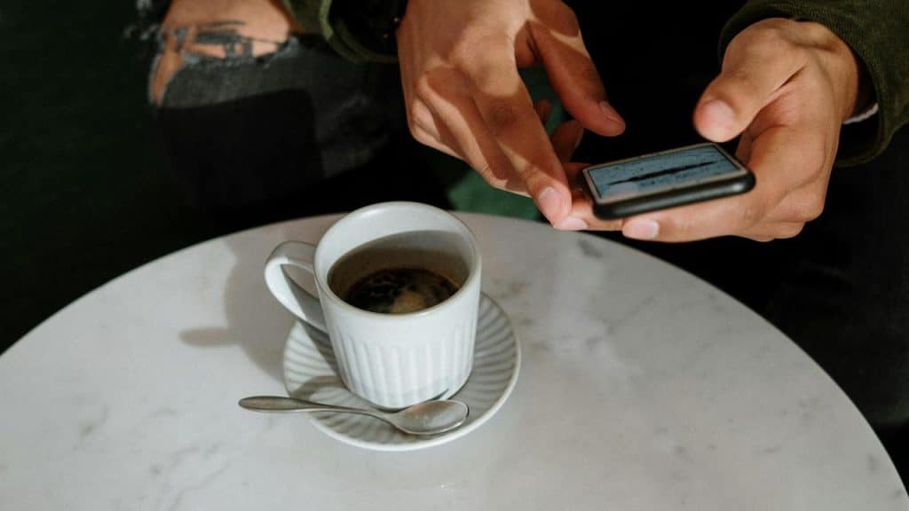 A person using a smartphone beside a cup of coffee on a table.