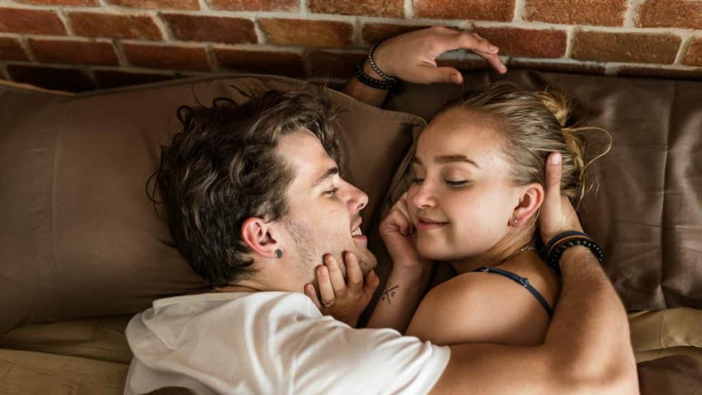 A couple lying in bed together smiling and embracing.
