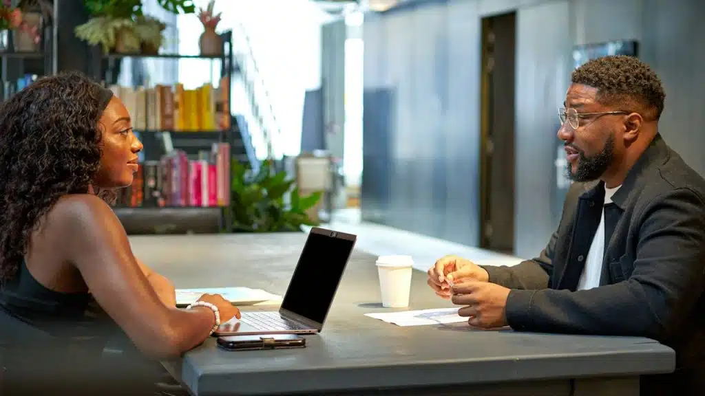 A woman and man sitting across a table from each other, engaged in a discussion in a modern office.Don’t 