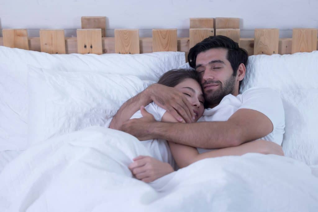 The couple is hugging each other in bed.