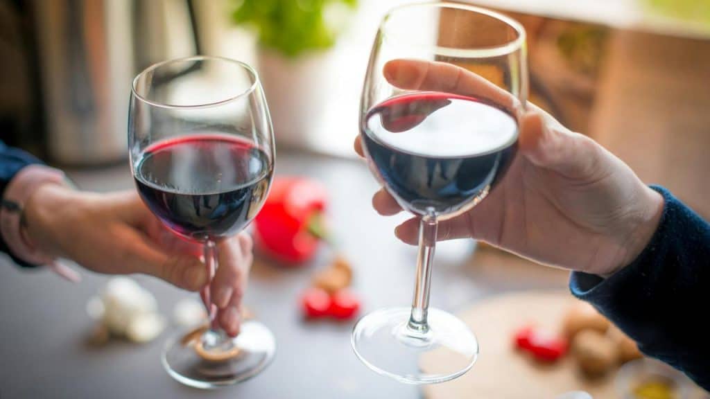A close-up of two people clinking glasses of red wine.