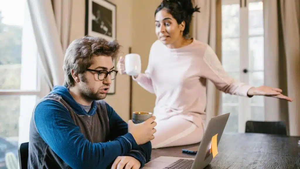 A woman gesturing in frustration while a man focuses on his laptop.