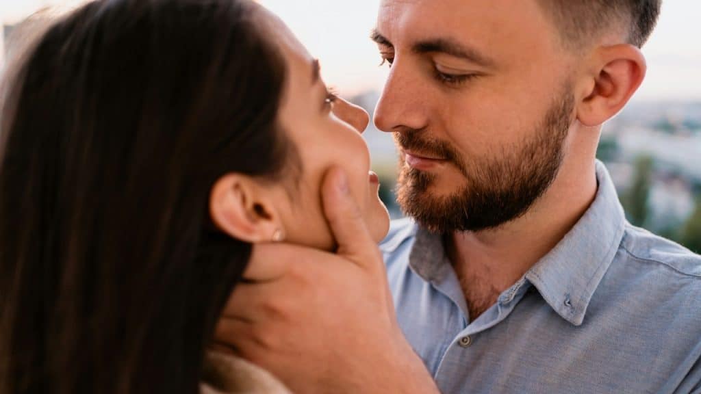 A smiling man holding a woman’s face.