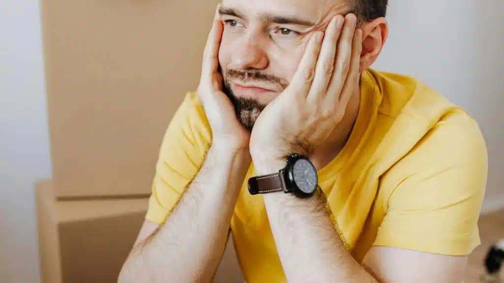 A man in a yellow shirt resting his face in his hands, looking thoughtful or tired.