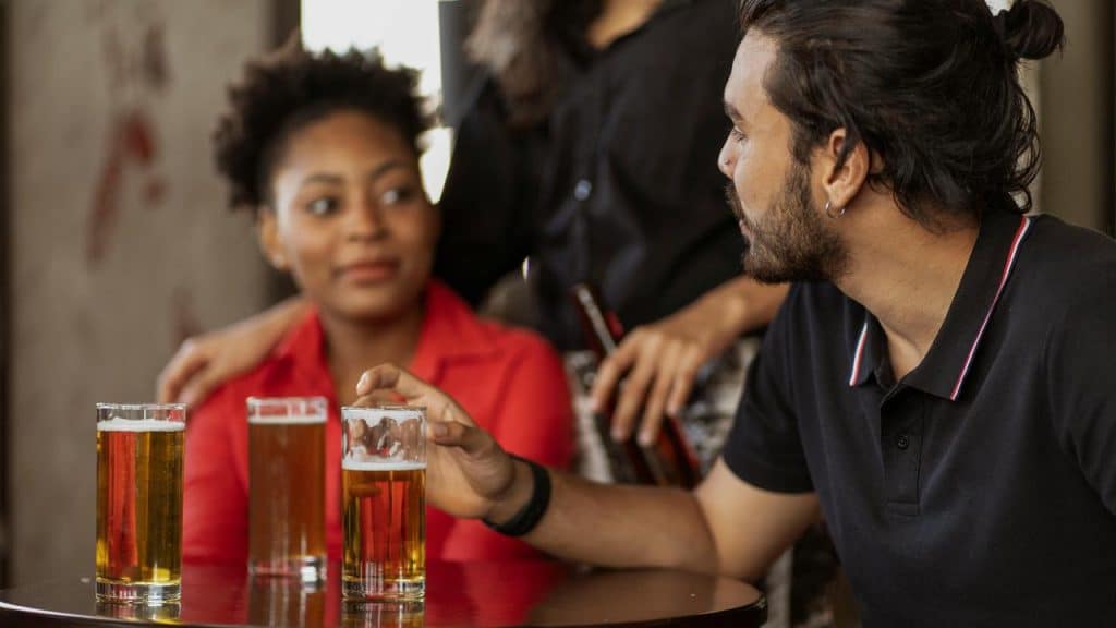 A man and woman talking at a table with glasses of beer.