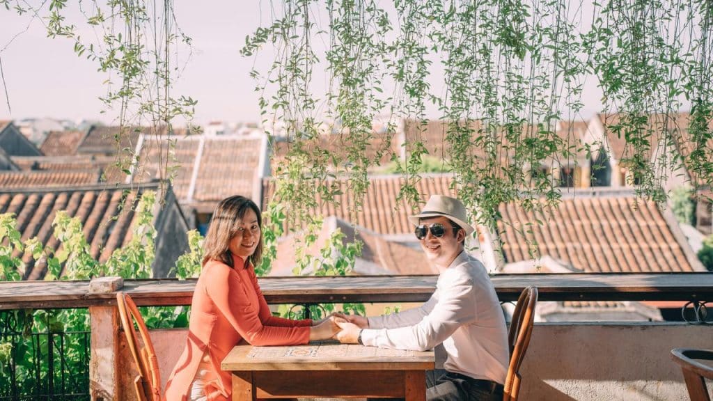 A smiling couple holding hands at an outdoor café with rooftop views.