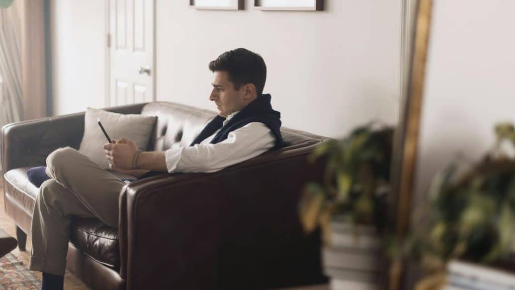 A man sitting on a couch and using a smartphone in a living room.